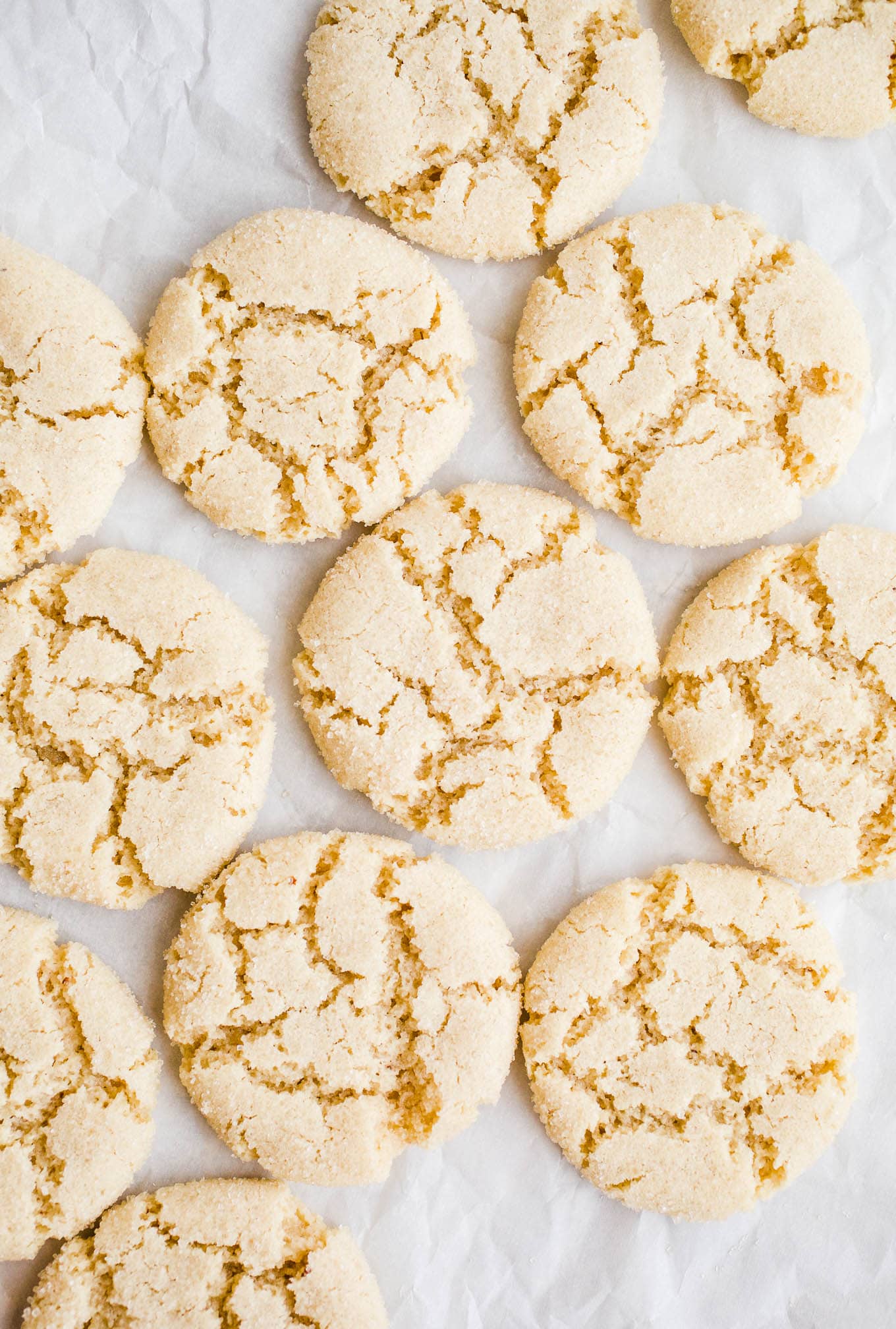 Soft and crackly almond cookies on white parchment paper.