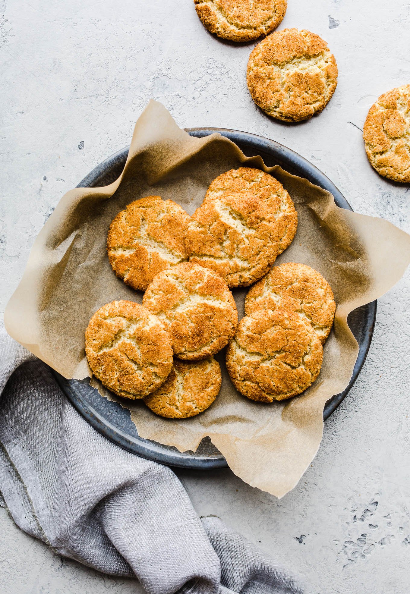 Snickerdoodle cookies on a piece of parchment paper on a blue tray.