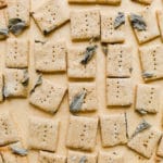 Crackers with pressed sage spread on a piece of parchment paper.
