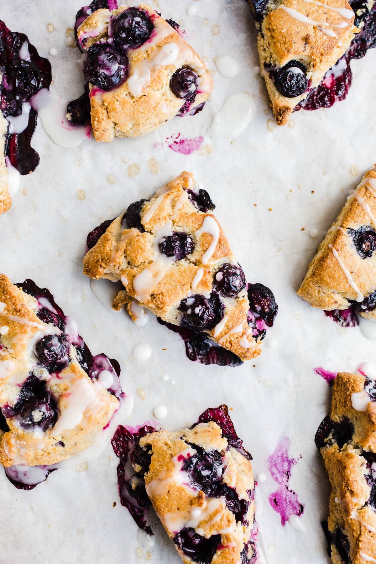 Blueberry scones with icing on parchment paper.