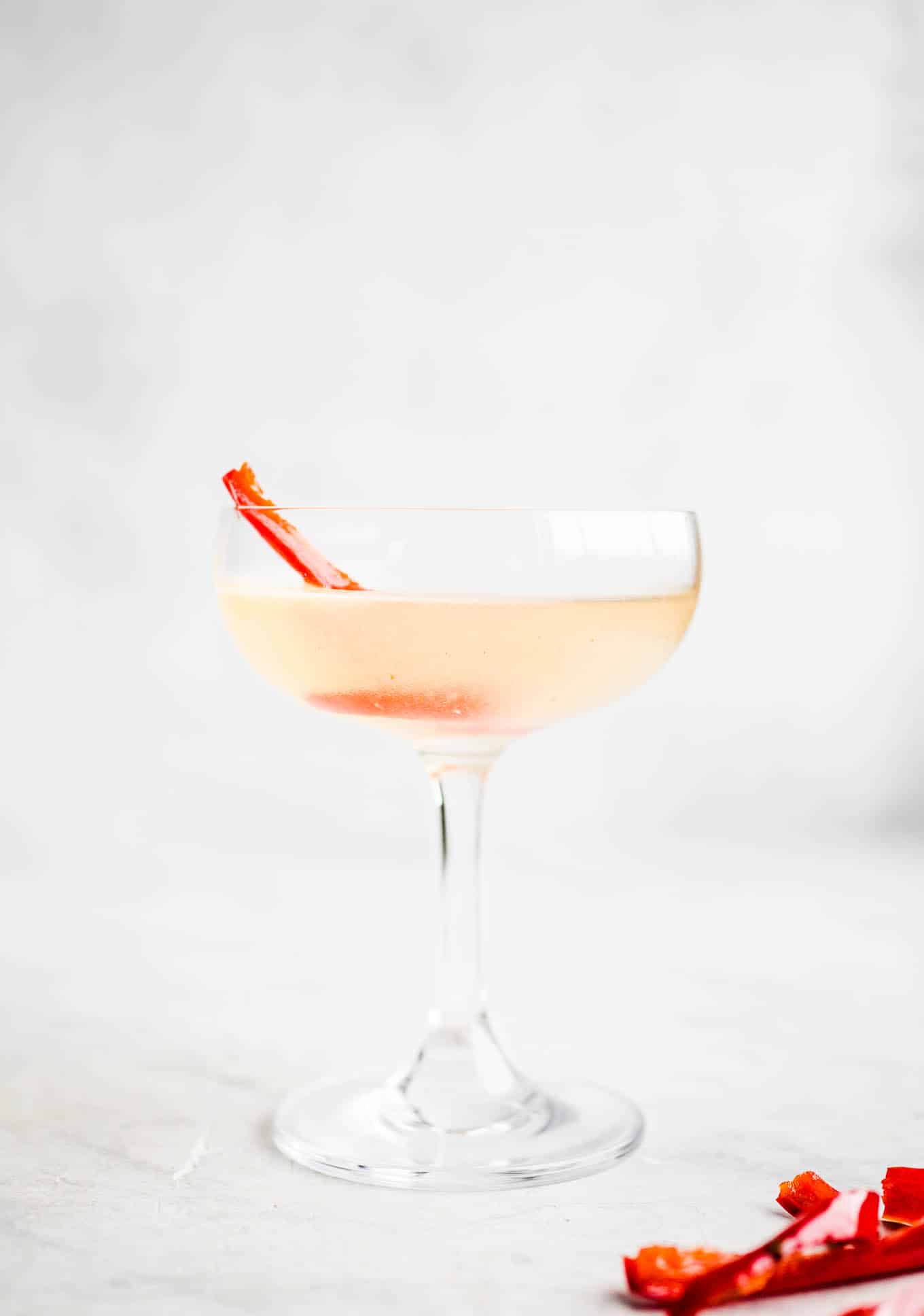 A coupe glass with filled with a light red drink.