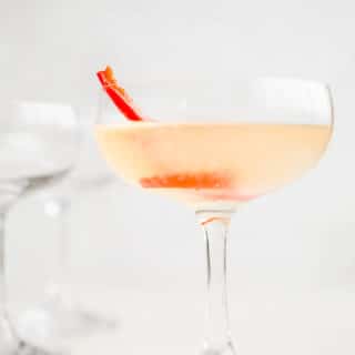 A coupe glass filled with a light red liquid.