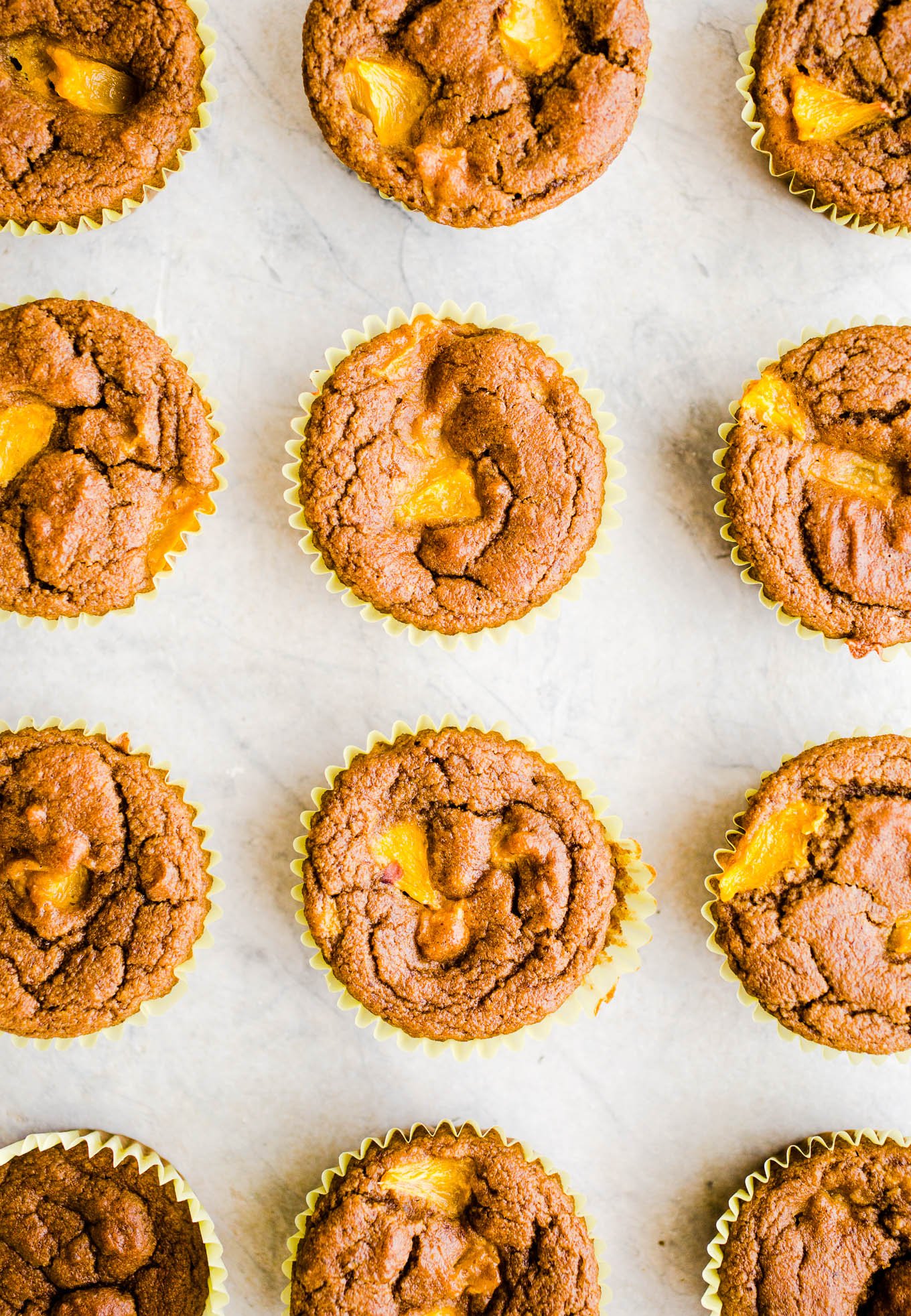 Fresh peach muffins on a marble surface.