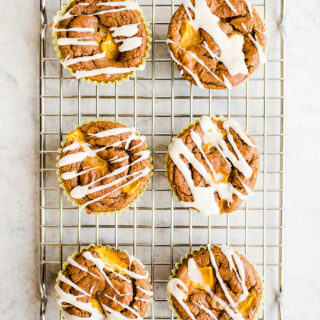 Peach muffins with icing on a rack.