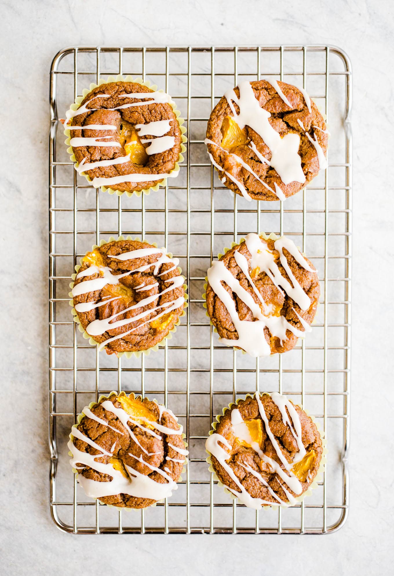 Peach muffins with icing on a rack.