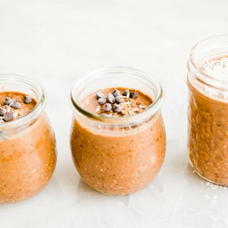 Chocolate peanut butter overnight oats with mini chocolate chips on top divided amongst three small glass jars.