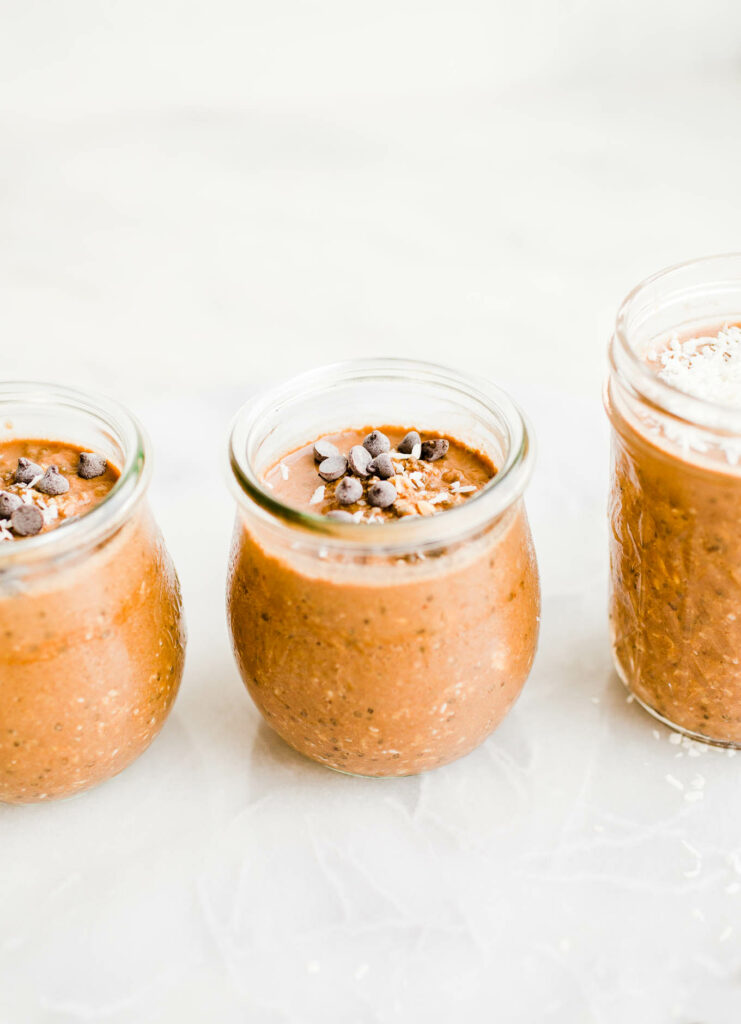 Chocolate peanut butter overnight oats with mini chocolate chips on top divided amongst three small glass jars.