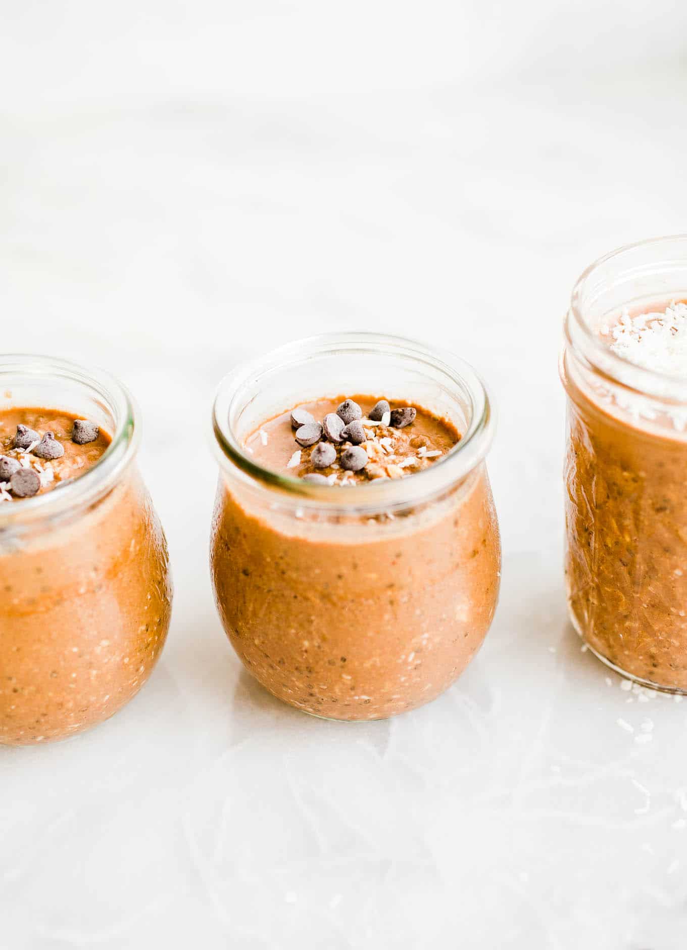 Chocolate peanut butter overnight oats with mini chocolate chips on top divided amongst three small glass jars.
