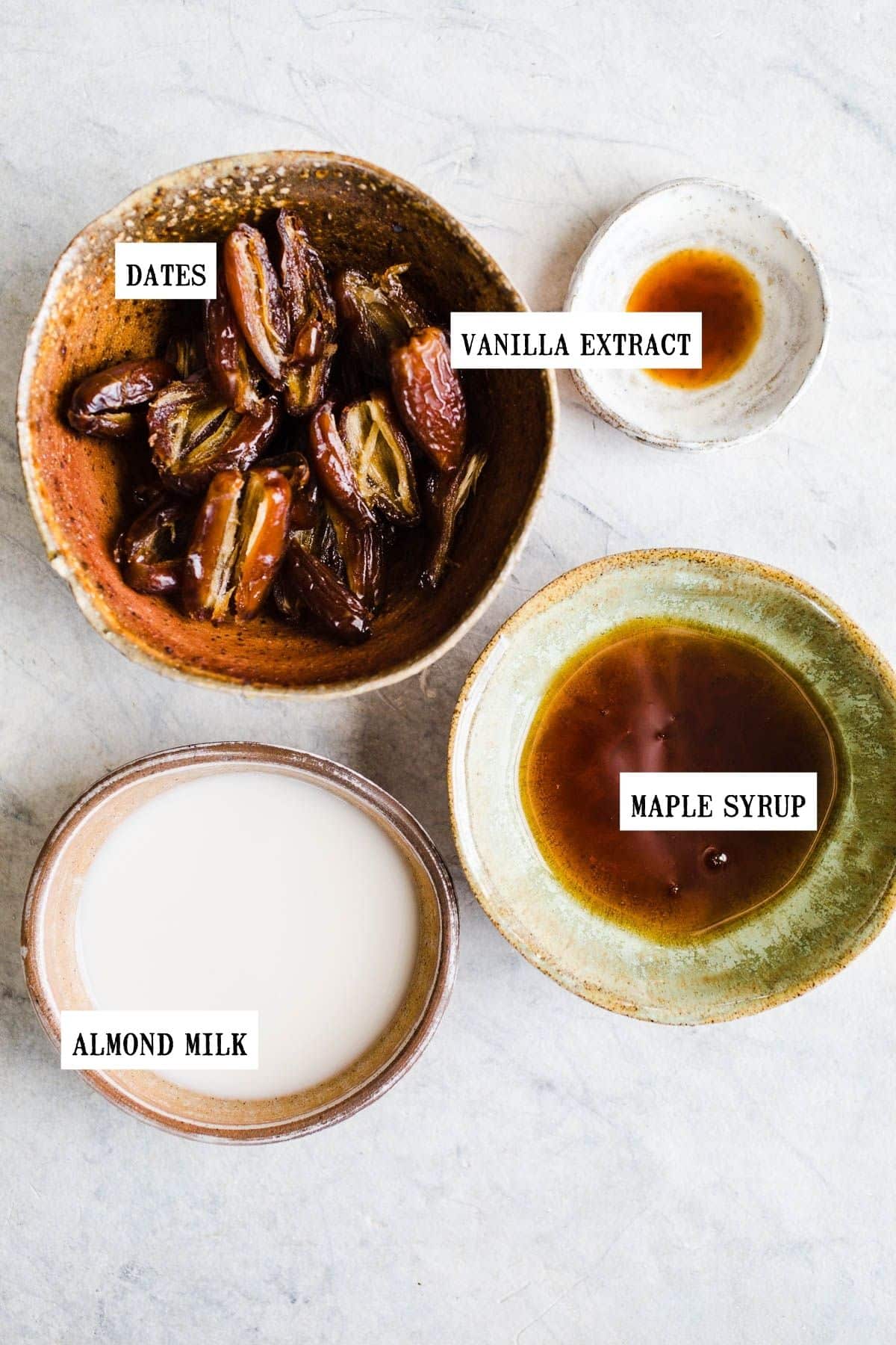 Dates, almond milk, maple syrup, and vanilla extract all in separate bowls.