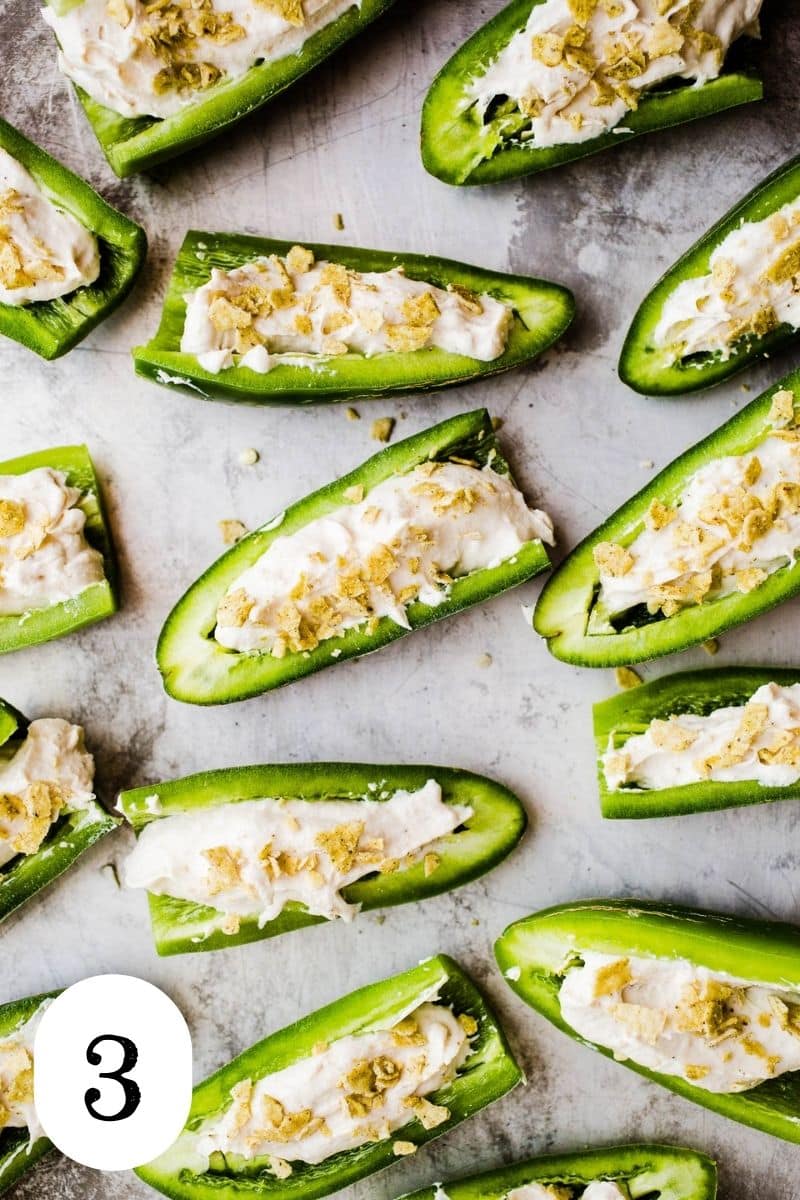 Cream cheese stuffed jalapenos with crushed potato chips on top sitting on a metal tray.