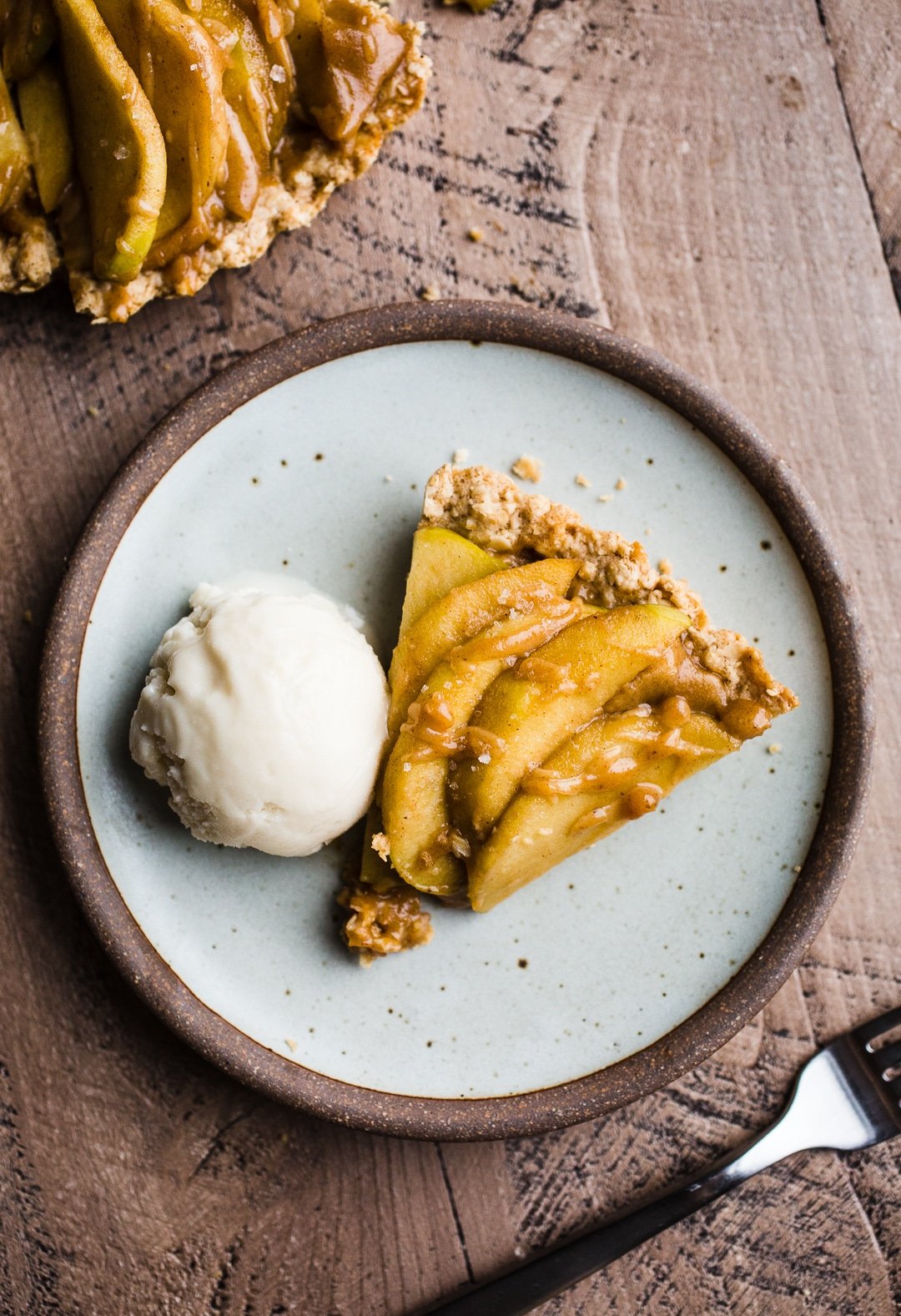 A slice of apple tart with a scoop of ice cream on a rustic plate. 