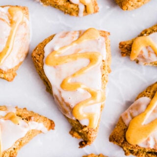 Pumpkin scones with vanilla and pumpkin glaze on white parchment paper.