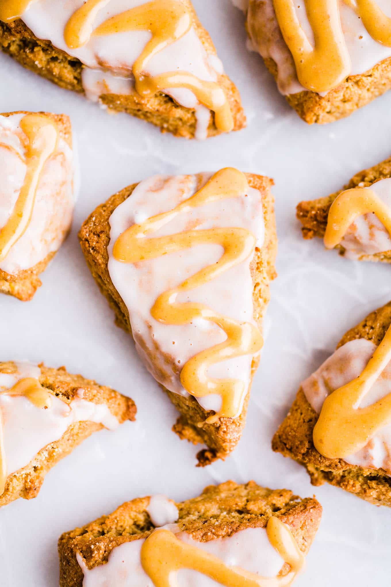 Pumpkin scones with vanilla and pumpkin glaze on white parchment paper.