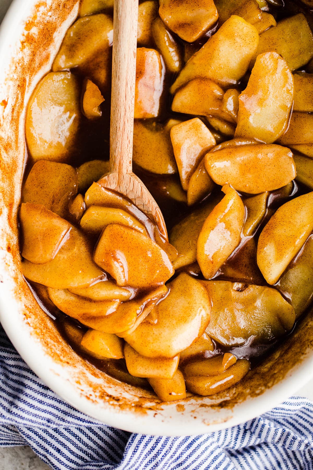 Cinnamon apples in syrup inside of a white baking dish with a wooden spoon.