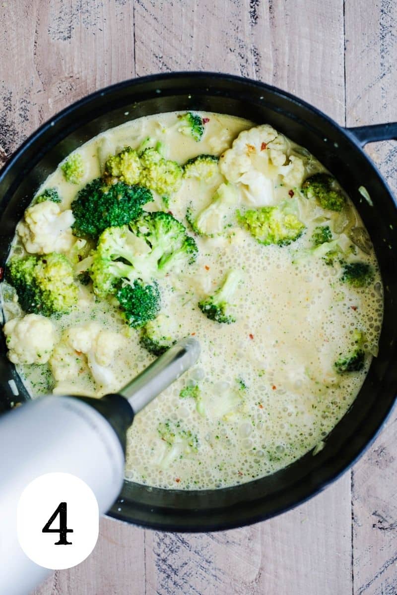 Broccoli cauliflower soup being pureed with an immersion blender in a Dutch oven.