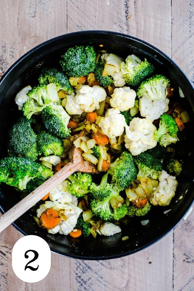 Broccoli and cauliflower being sauteed with onions and carrots in a Dutch oven.