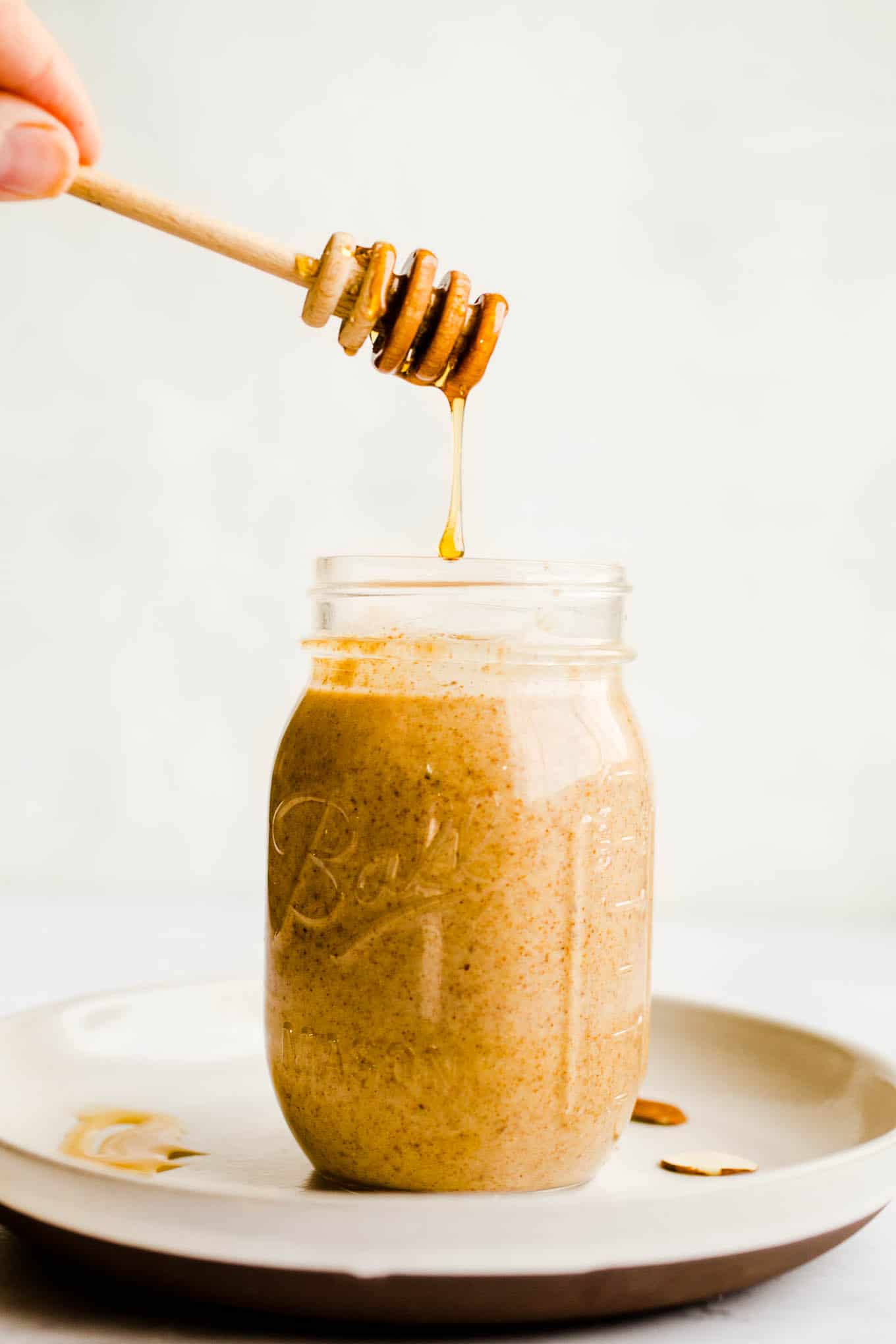 Honey being drizzled into a mason jar filled with almond butter. 