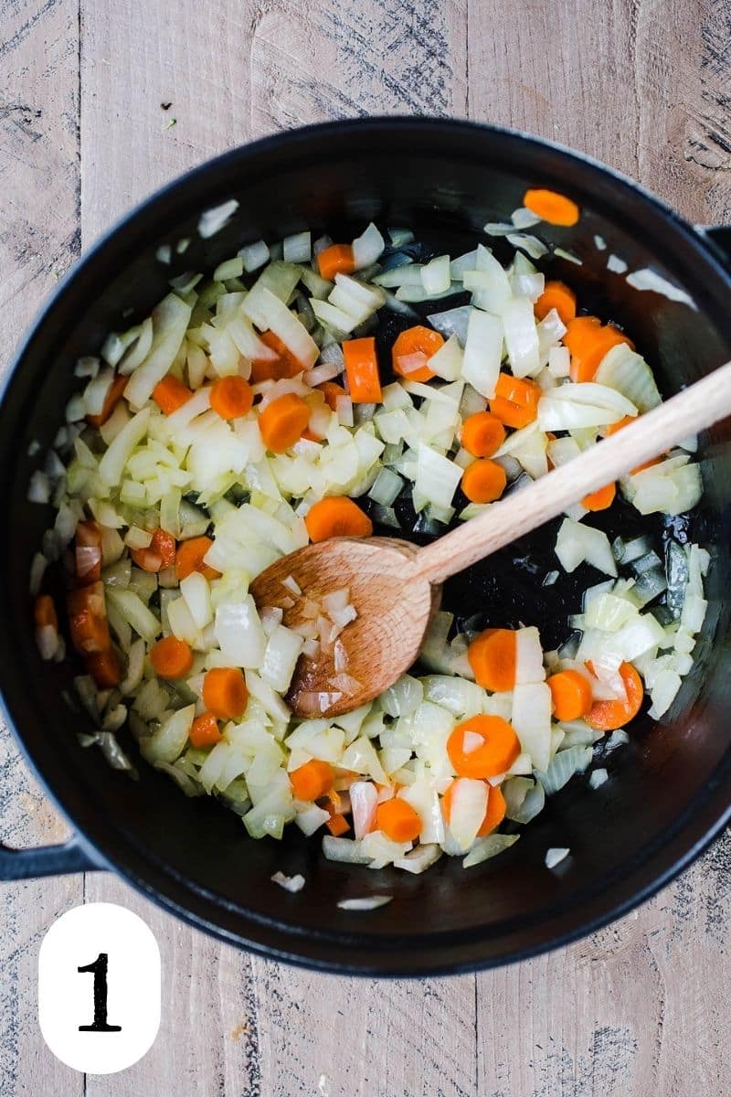 Carrots and onions being sauteed in a black Dutch oven. 