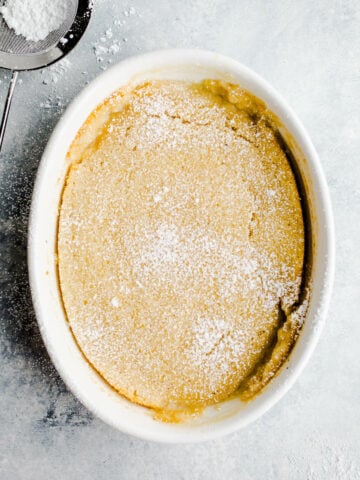 Yellow cake in a white baking dish sprinkled with powder sugar.