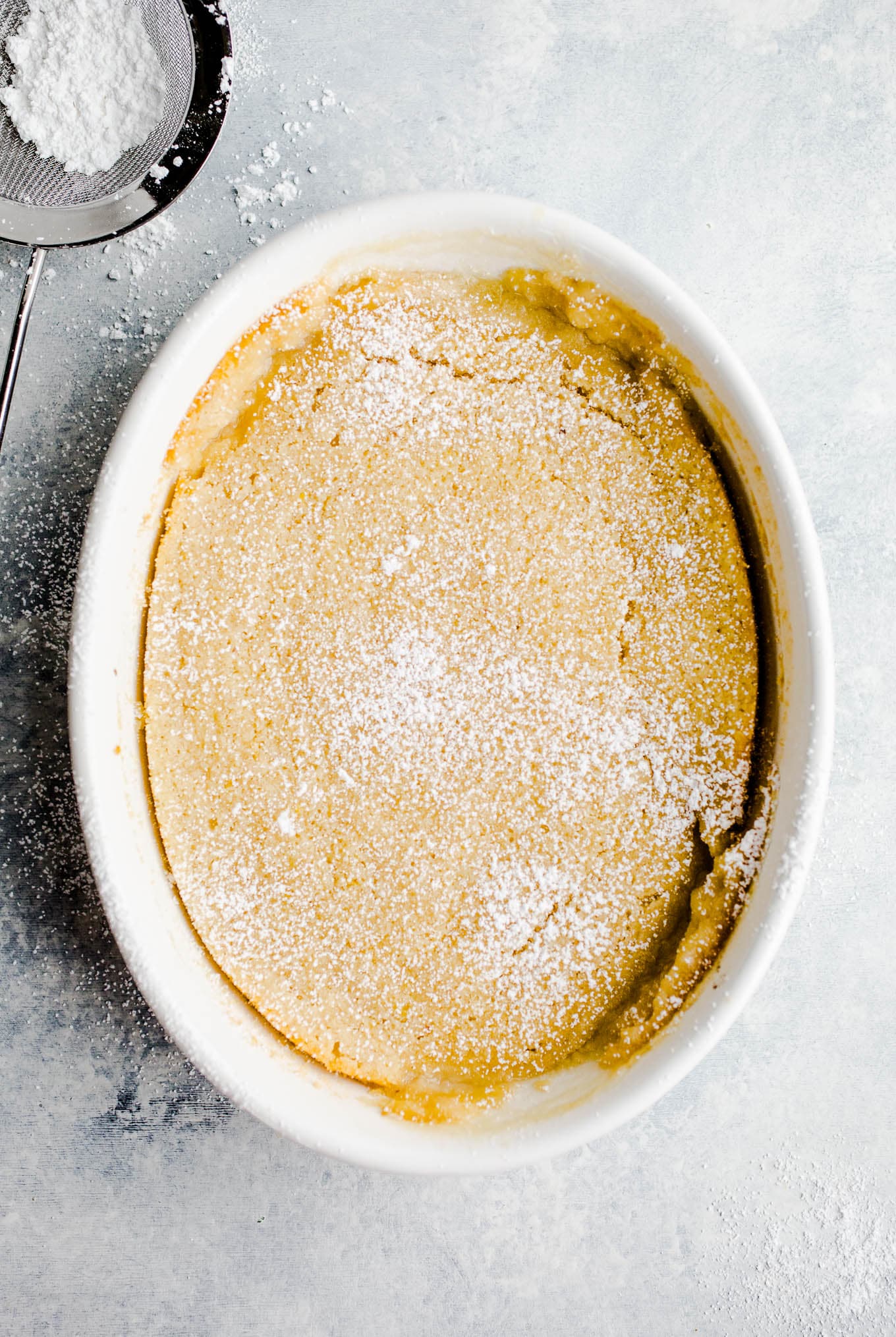 Yellow cake in a white baking dish sprinkled with powder sugar.