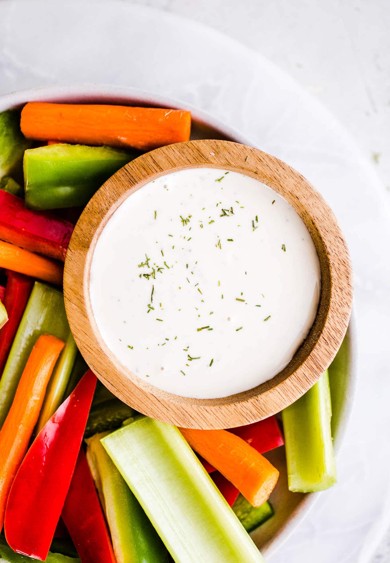 Celery, carrots, and peppers on a plate with a cup of dressing. 