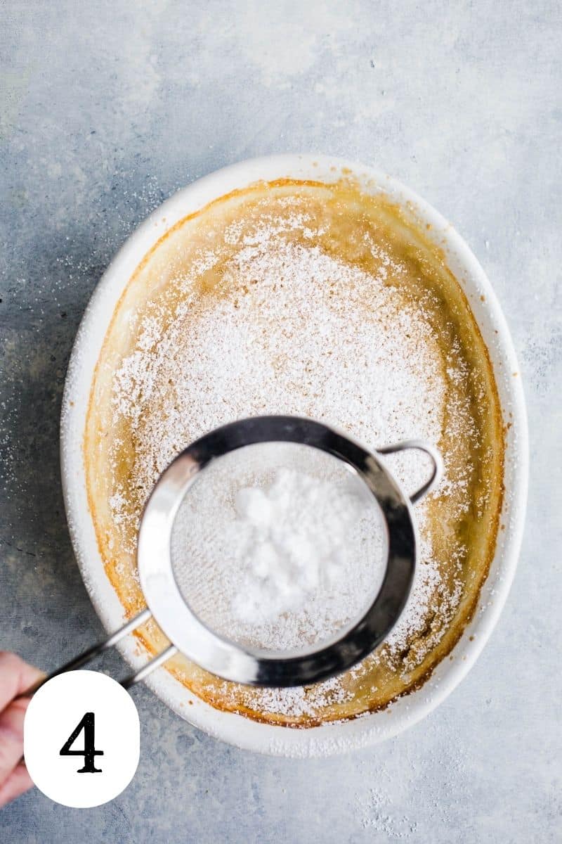 Powdered sugar being sprinkled over warm cake in a white dish.