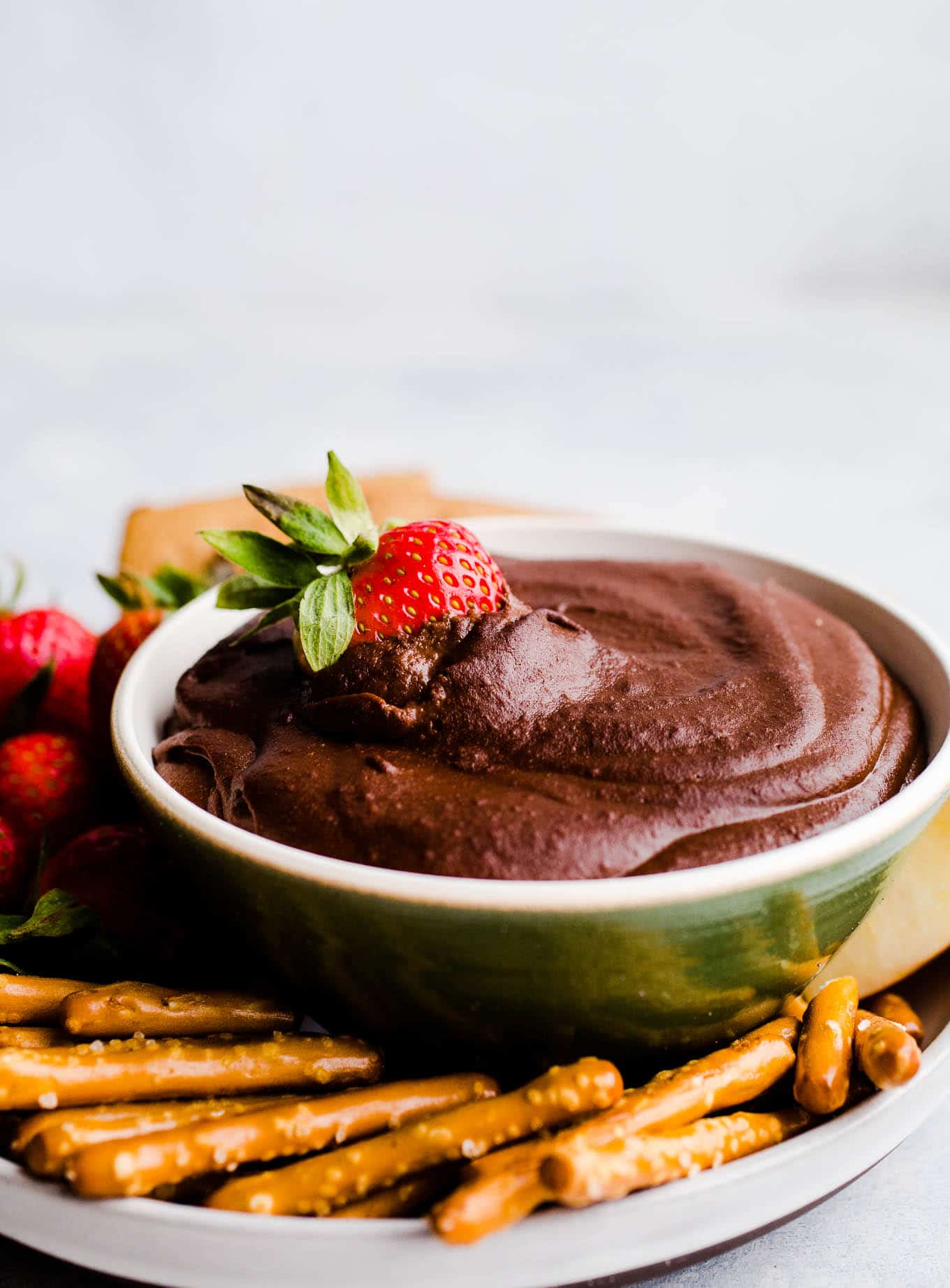 Chocolate dip in a bowl with strawberries and pretzels.