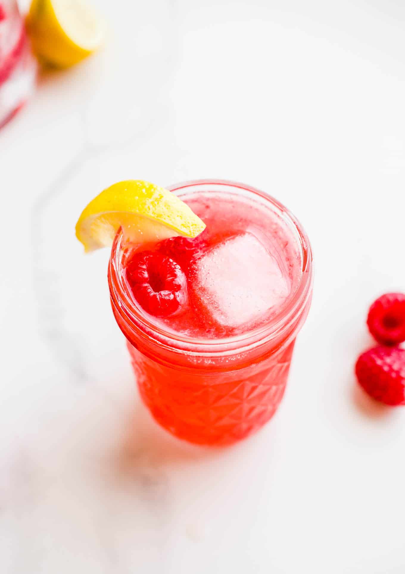 A raspberry and vodka cocktail in a mason jar with a lemon wedge.