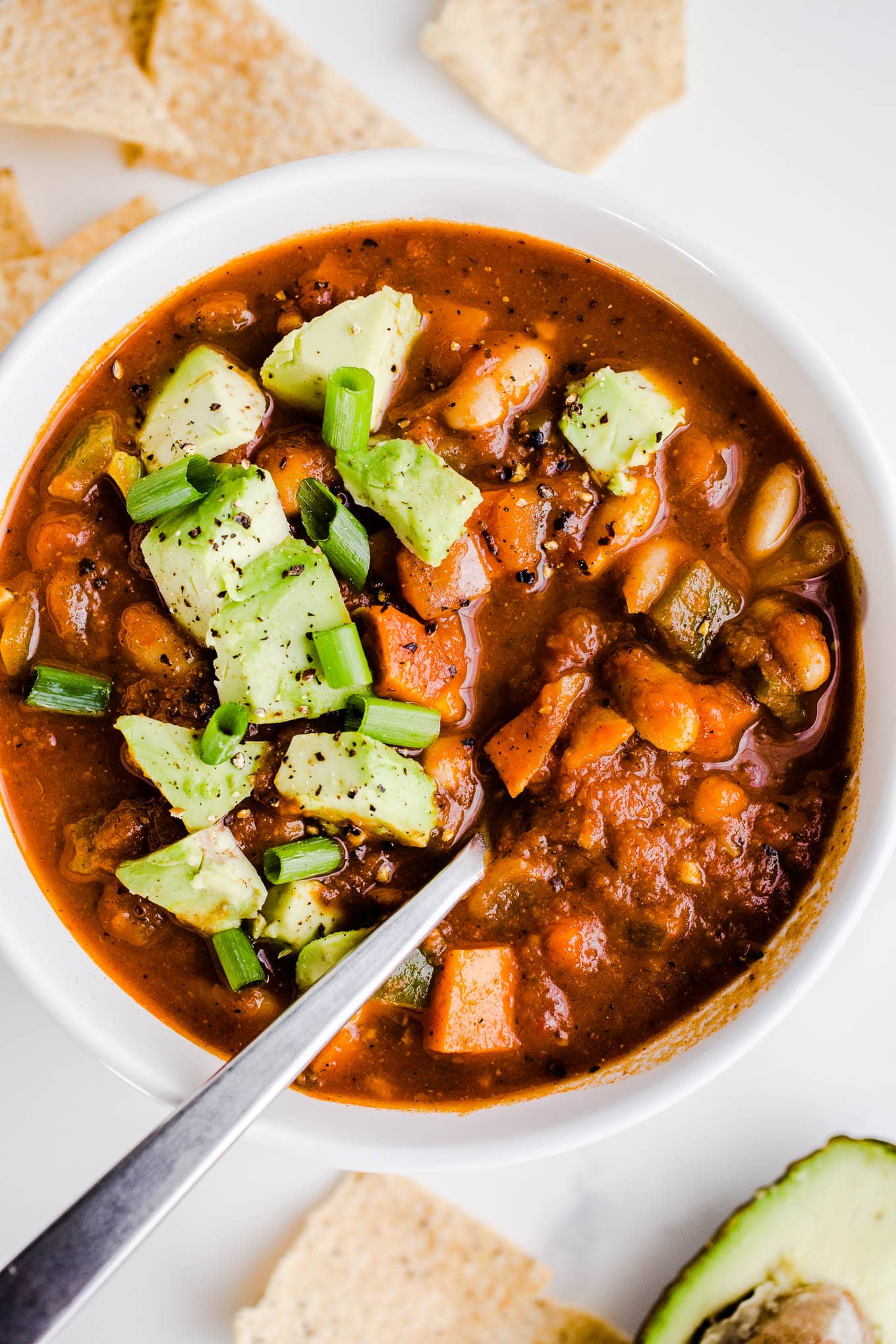 Pumpkin chili with sweet potatoes and chopped avocado on top in a white bowl.