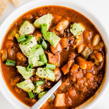Vegetarian chili with avocado in a white bowl with a silver spoon.