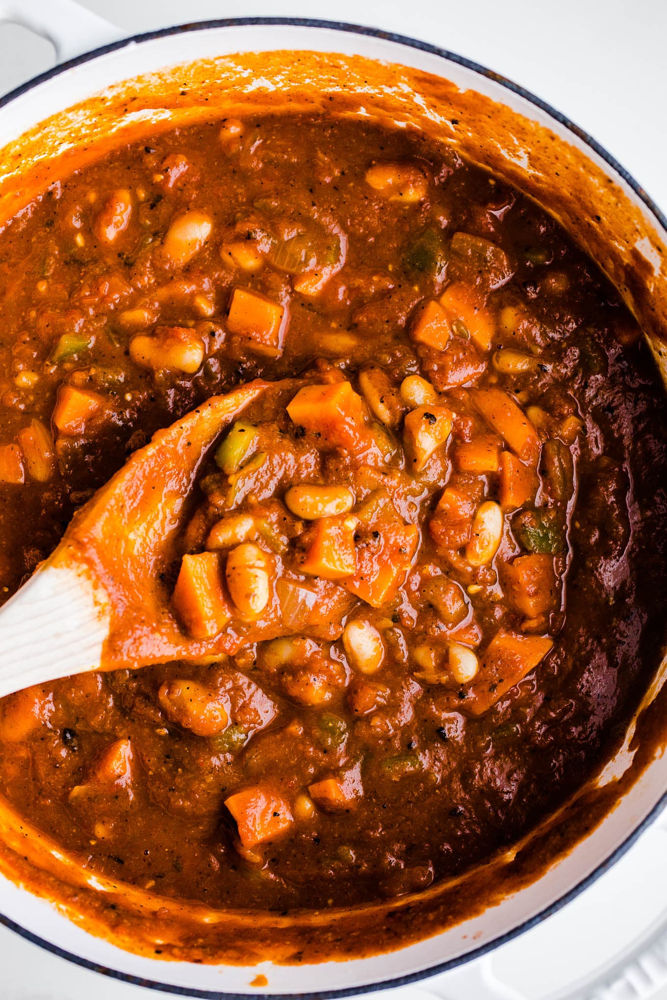 Pumpkin chili in a large white pot being stirring with a wooden spoon.