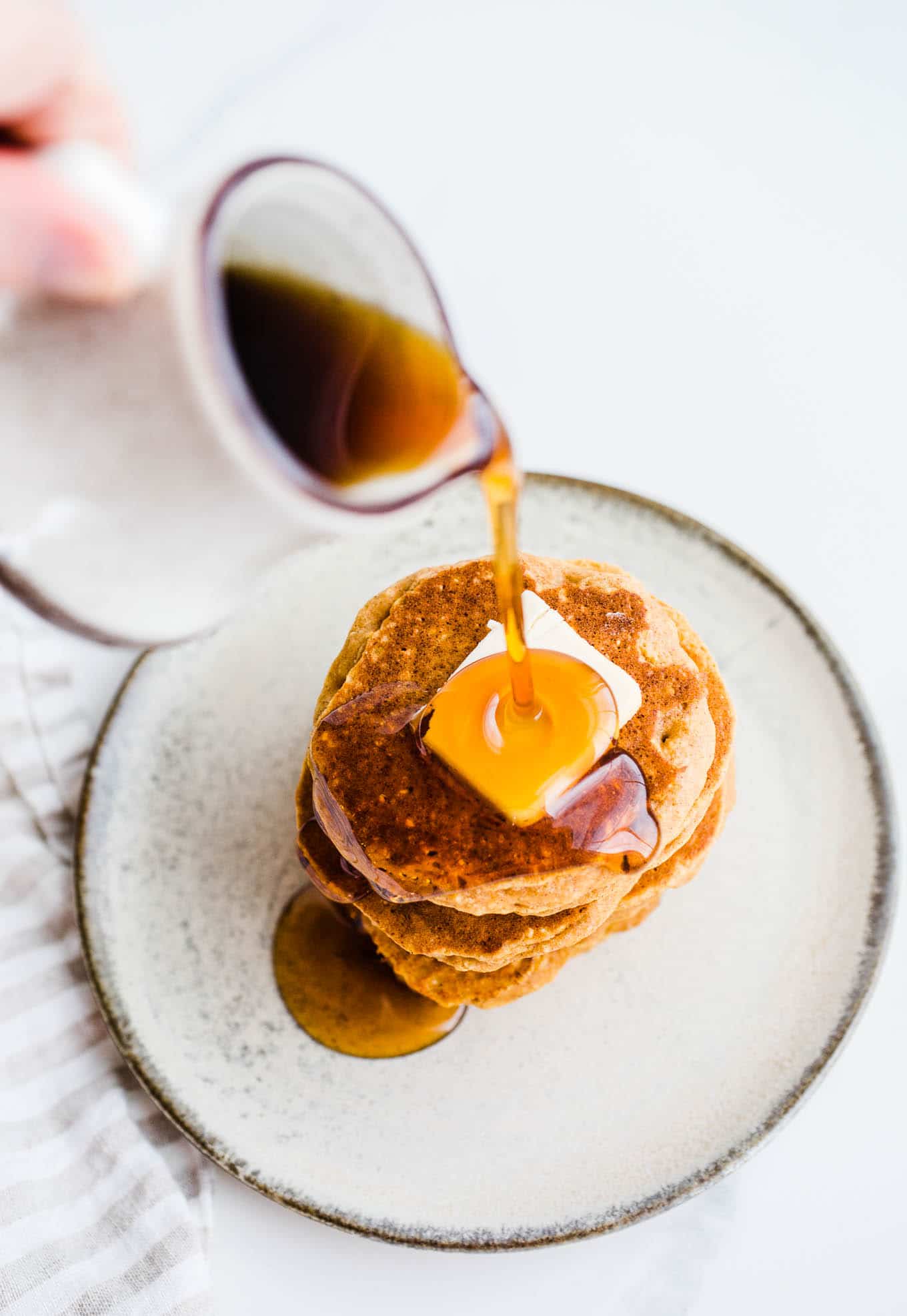 Syrup being poured over a stack of pancakes.