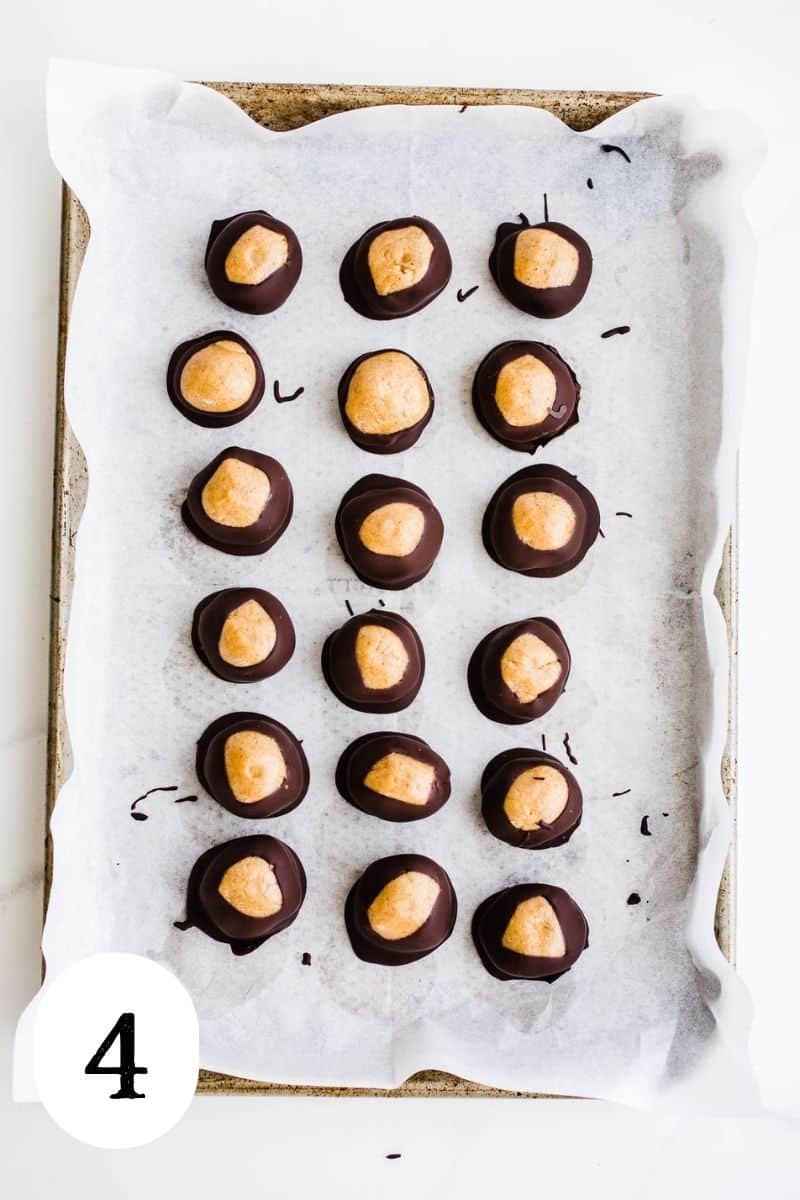 Peanut butter balls coated in chocolate on a baking sheet.