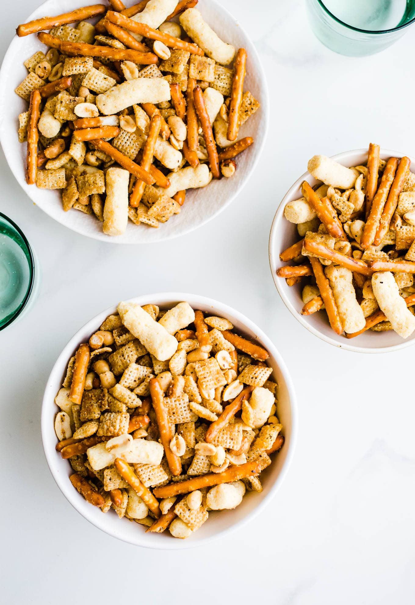 pretzels, peanuts, chex, and cheese puffs in white bowls