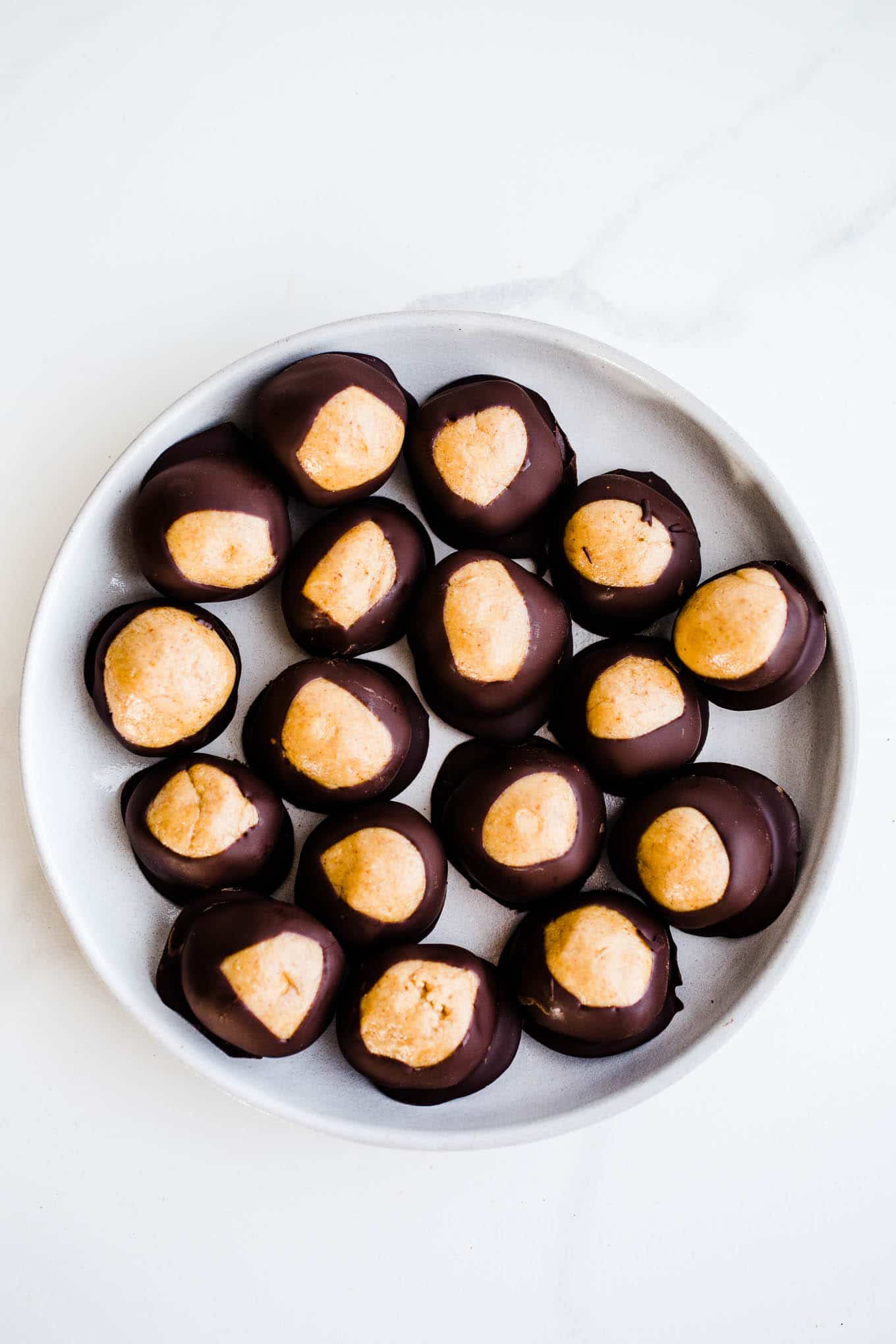 Peanut butter chocolate buckeyes on a white plate set on a marble surface.