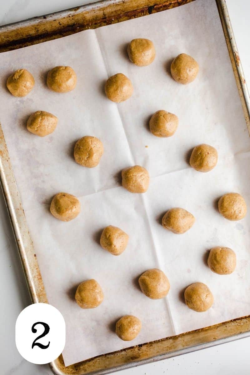 Peanut butter balls in rows on a parchment-lined baking sheet.