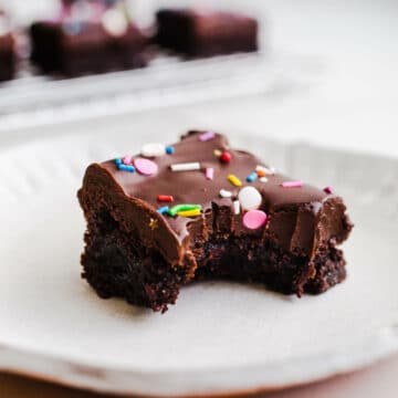 a cosmic brownies with fudge ganache and sprinkles on a white plate.