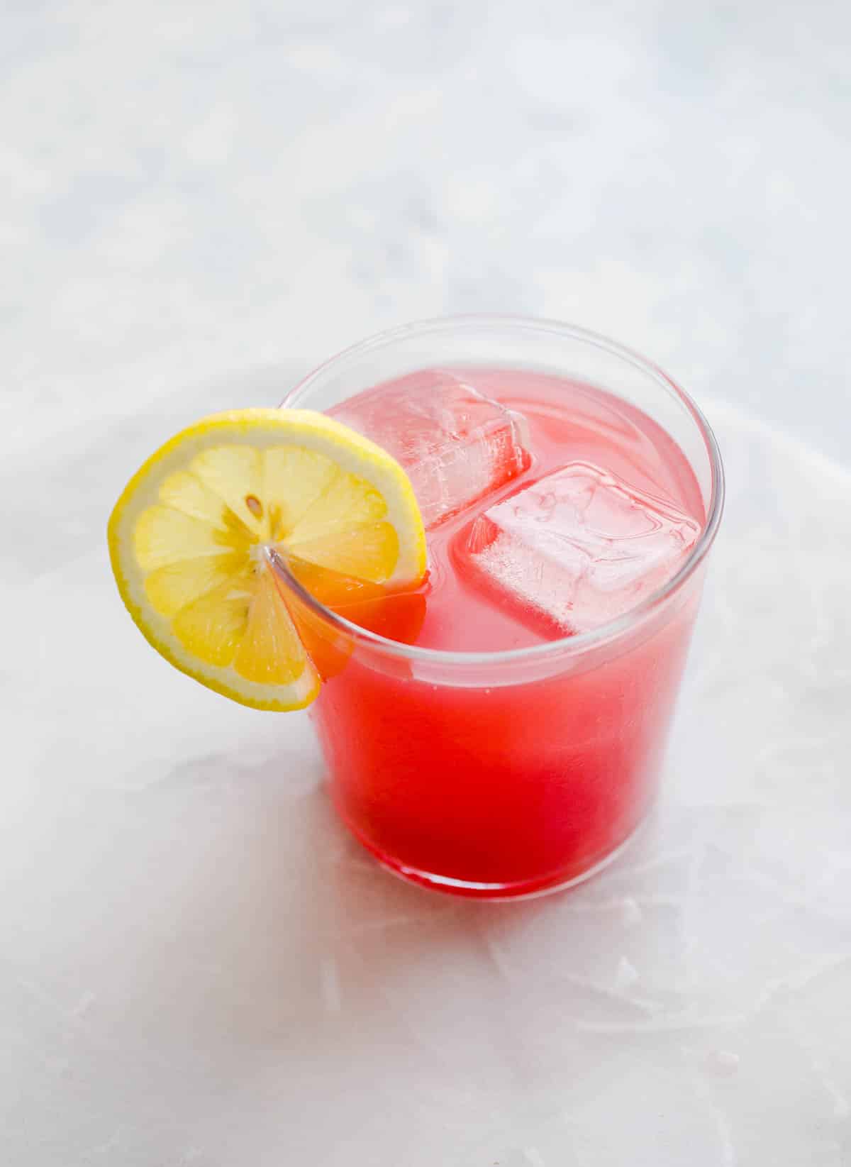Bright pink grapefruit hibiscus cocktail in a glass with ice and a lemon wheel.