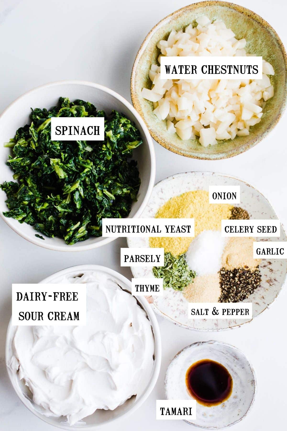 Ingredients for spinach dip in small bowls including spinach, water chestnuts, spices, sour cream, and tamari.