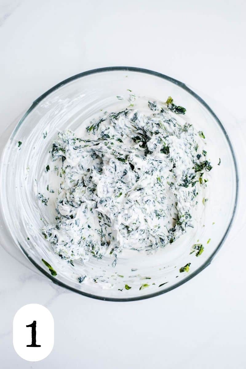 Sour cream and chopped spinach that have been combined in a medium glass bowl.