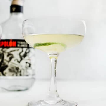A coupe glass filled with a tequila mixture with a lime wheel as a garnish.