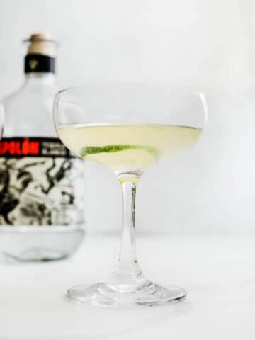 A coupe glass filled with a tequila mixture with a lime wheel as a garnish.