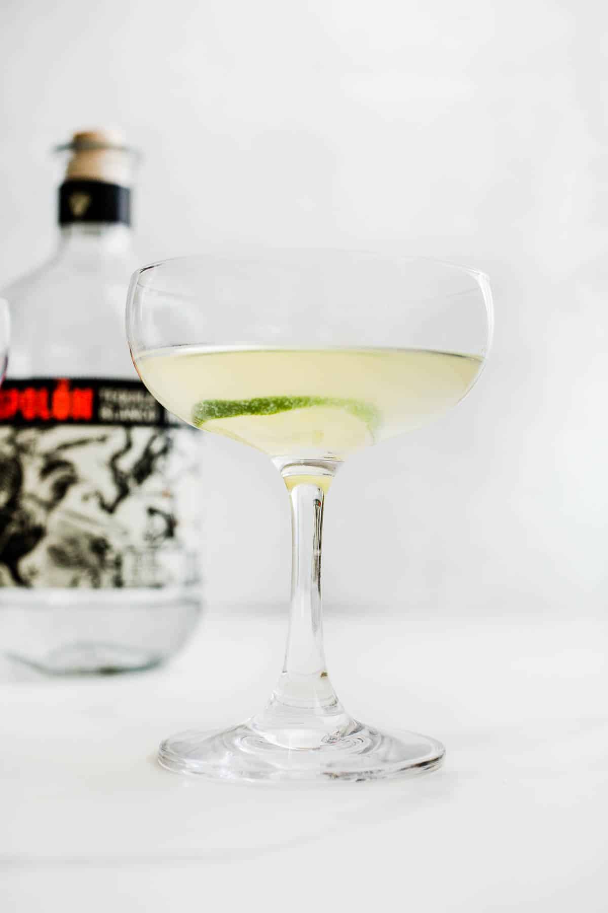 A tequila gimlet in a coupe cocktail glass with a lime wheel as garnish.