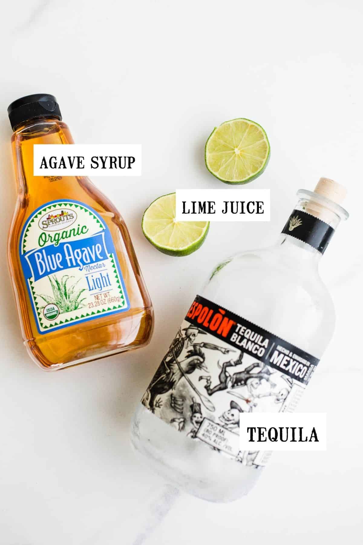 A bottle of agave nectar, tequlia blanco, and two lime halves on a marble counter.