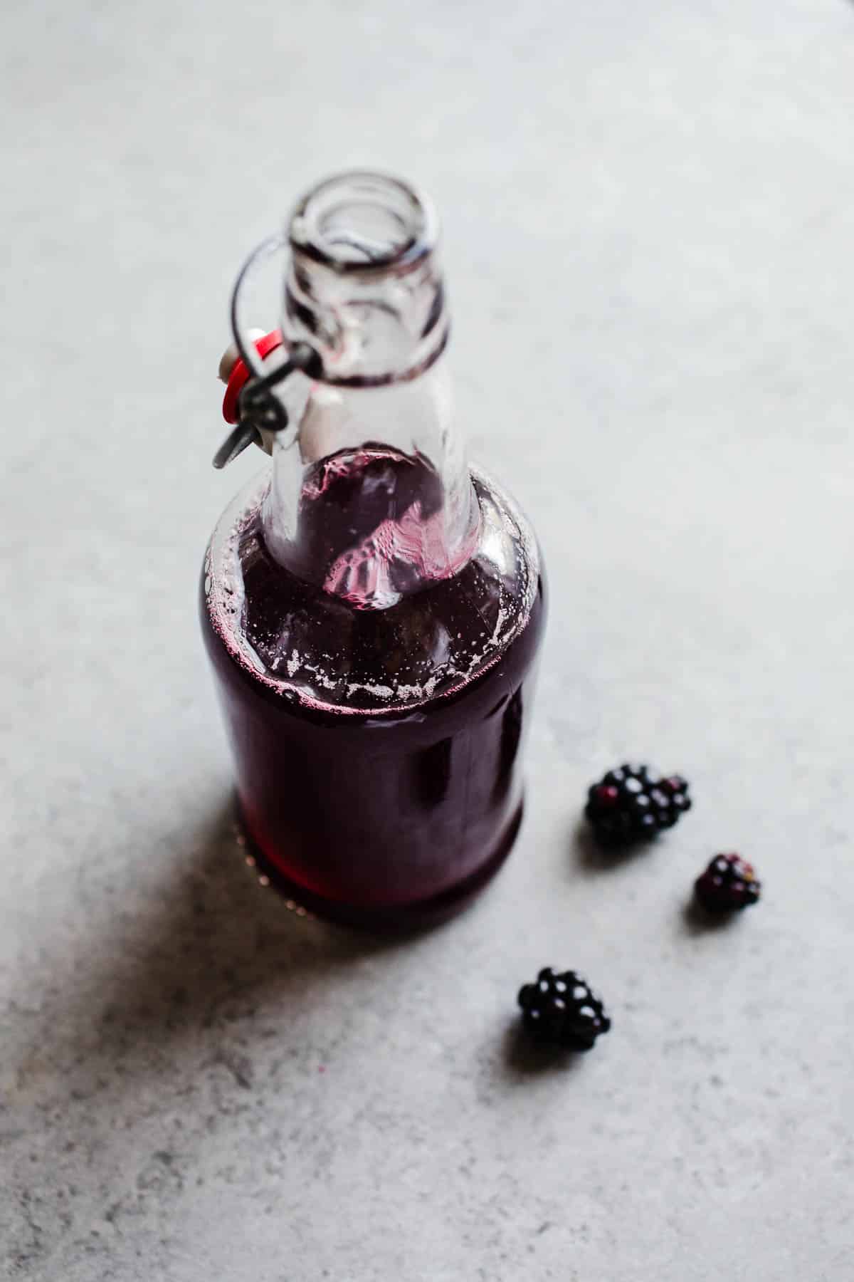 A glass bottle containing blackberry simple syrup with the lid popped open.