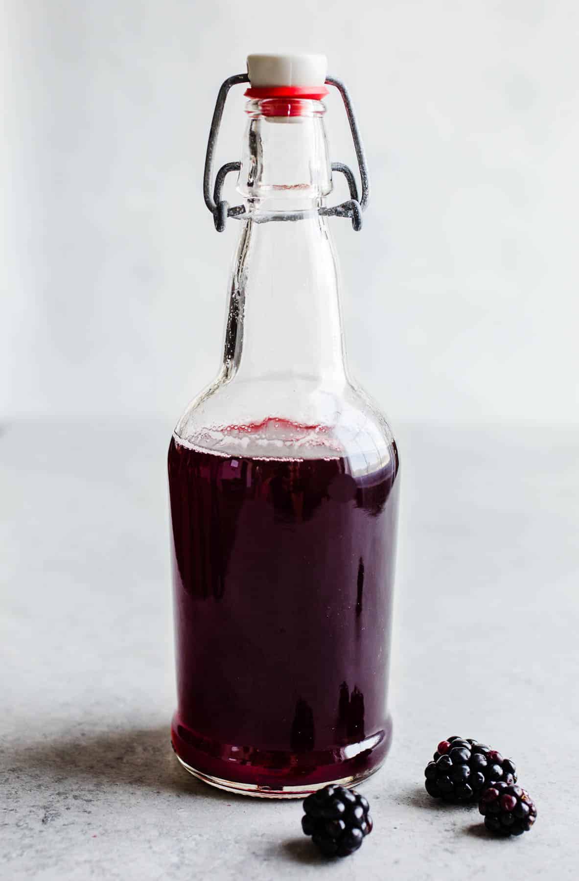 Una botella de vidrio con una tapa blanca y roja llena de jarabe simple de mora. 