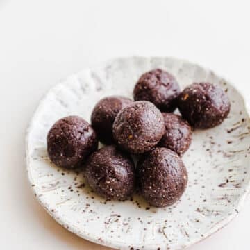 Eight small chocolate date balls on a small speckled white plate.