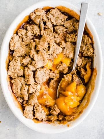 Baked peaches topped with oat flour crumble topping in a white baking dish.