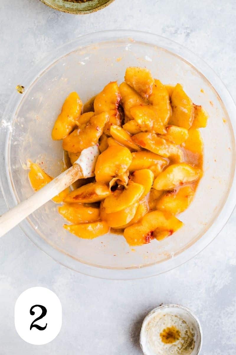 Peaches mixed with arrowroot and spices into a syrupy mixture in a glass mixing bowl. 