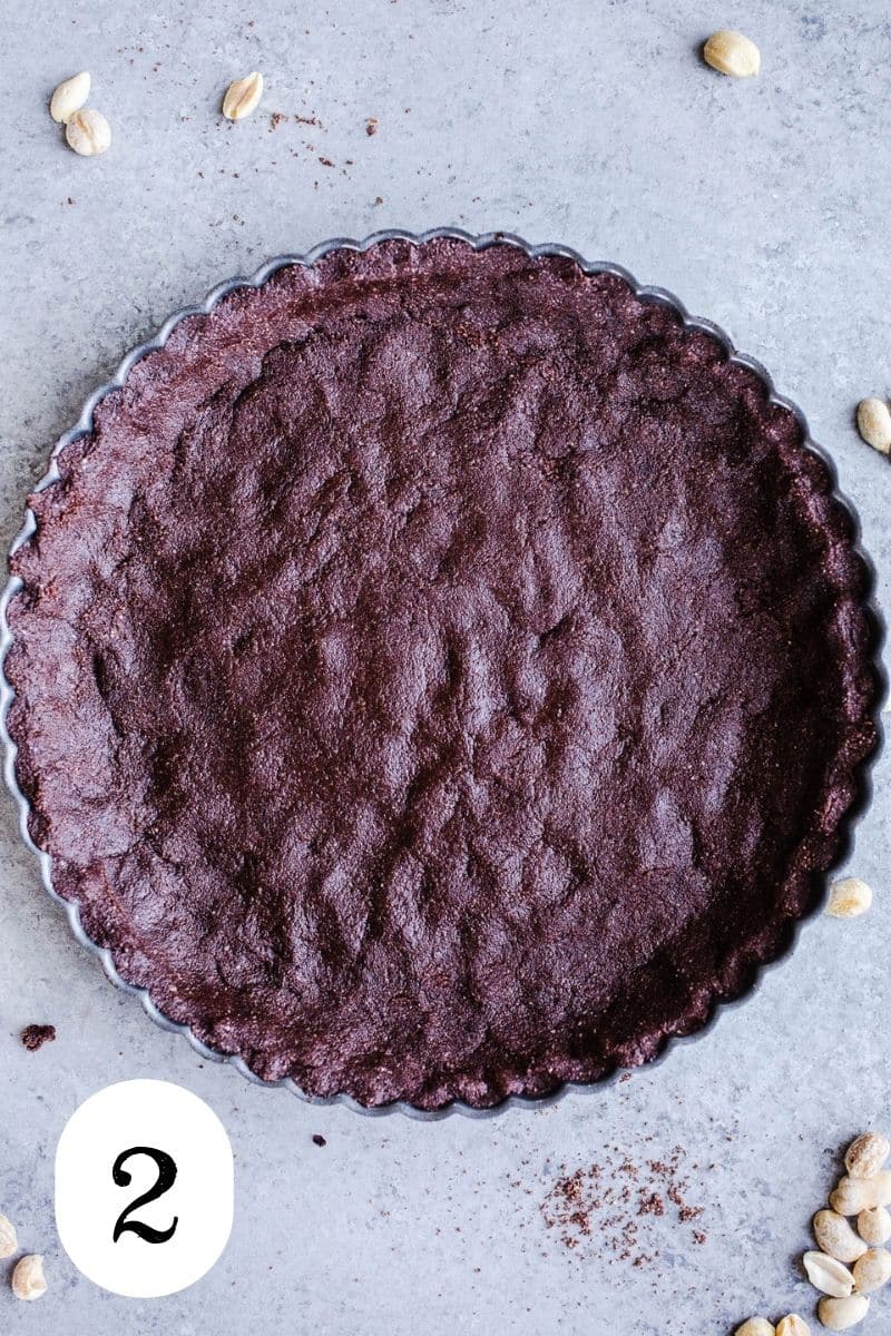 Chocolate almond flour crust pressed into a tart pan sitting on a gray surface.